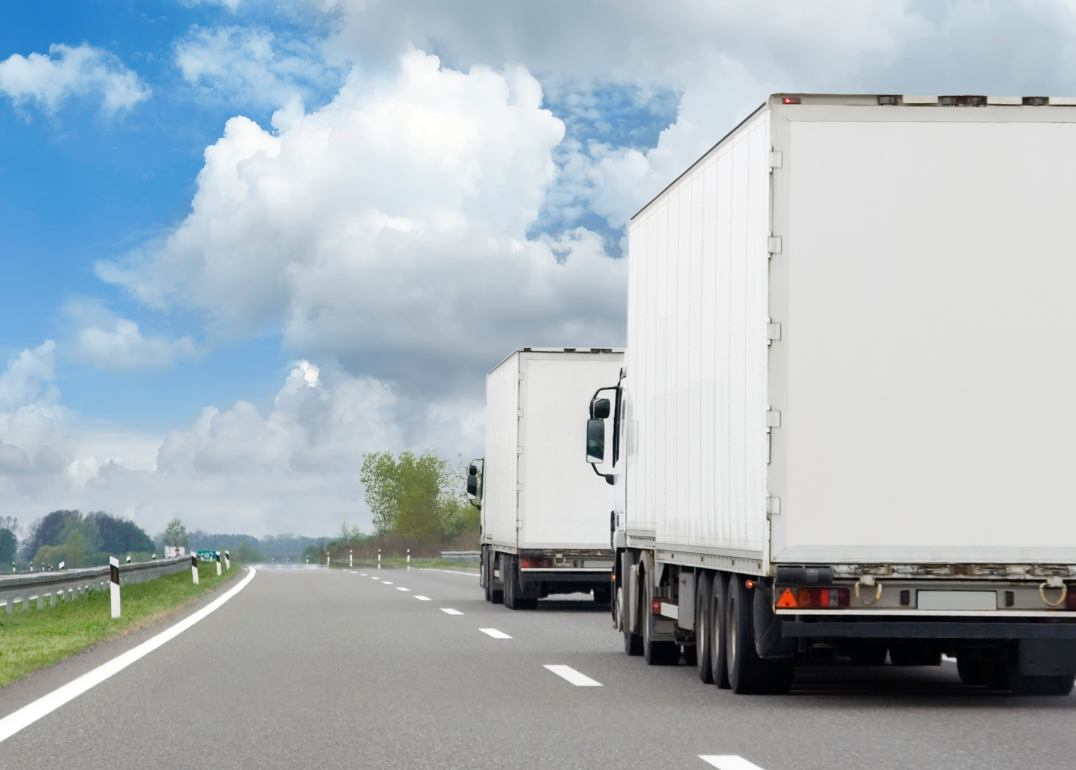 Delivery trucks on a road lined with green trees